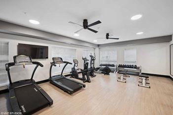 a gym with cardio machines and a ceiling fan